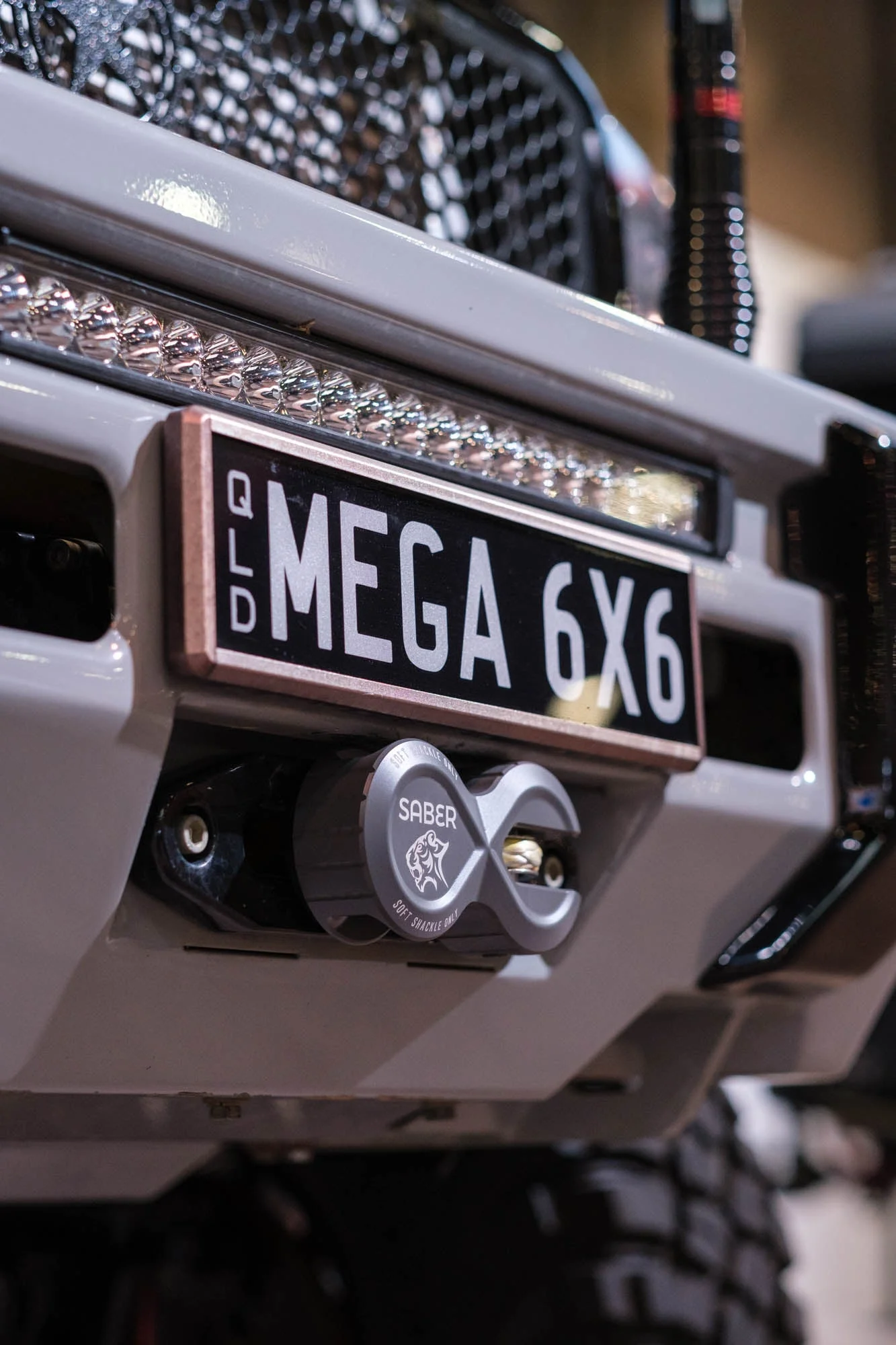 Close-up of a silver Saber alloy winch shackle mounted on The Mega 6x6's front bumper, with the QLD 'MEGA 6X6' number plate visible