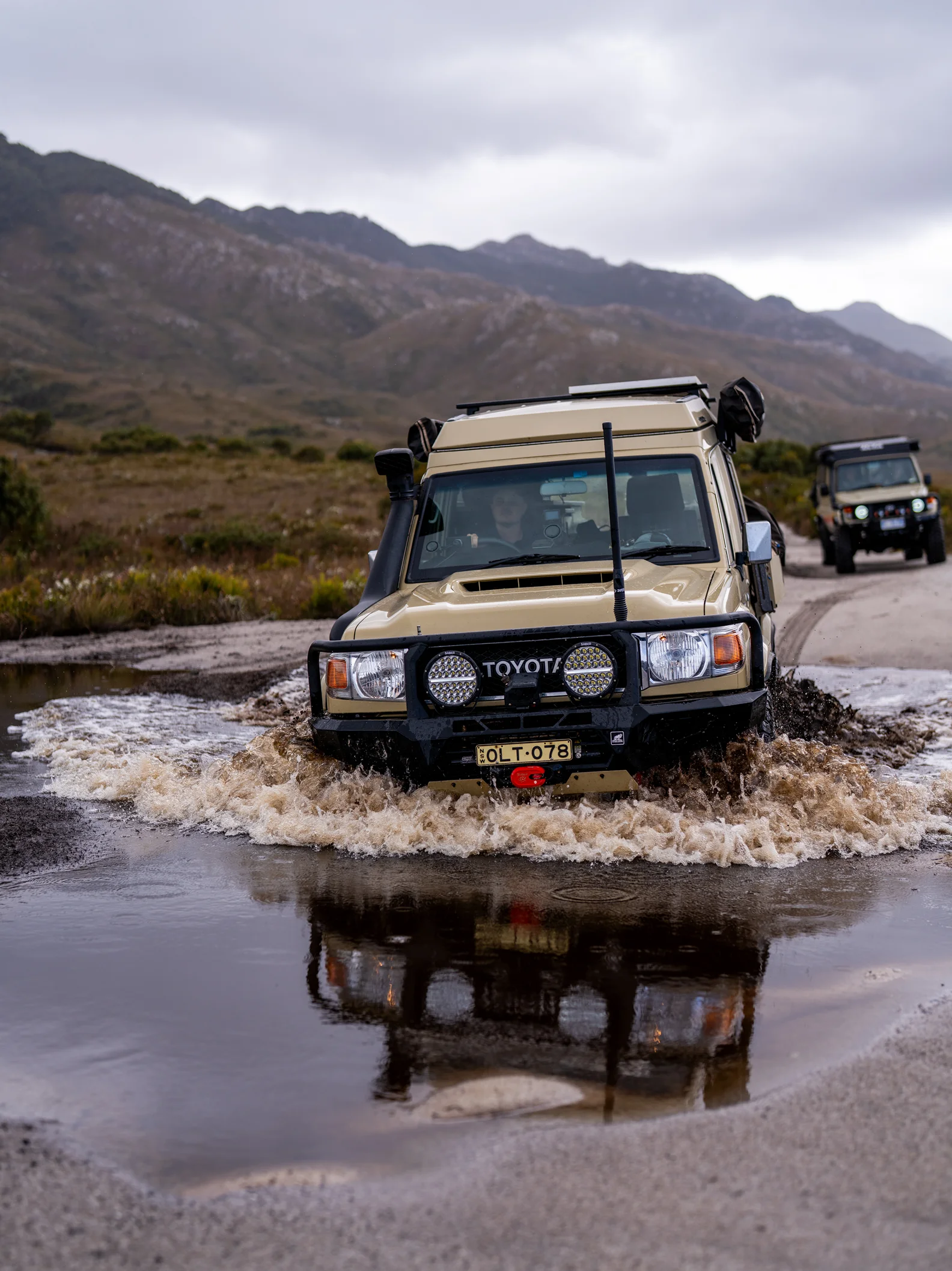 Convoy of 4WDs crossing a shallow water ford on a mountain track, kicking up spray