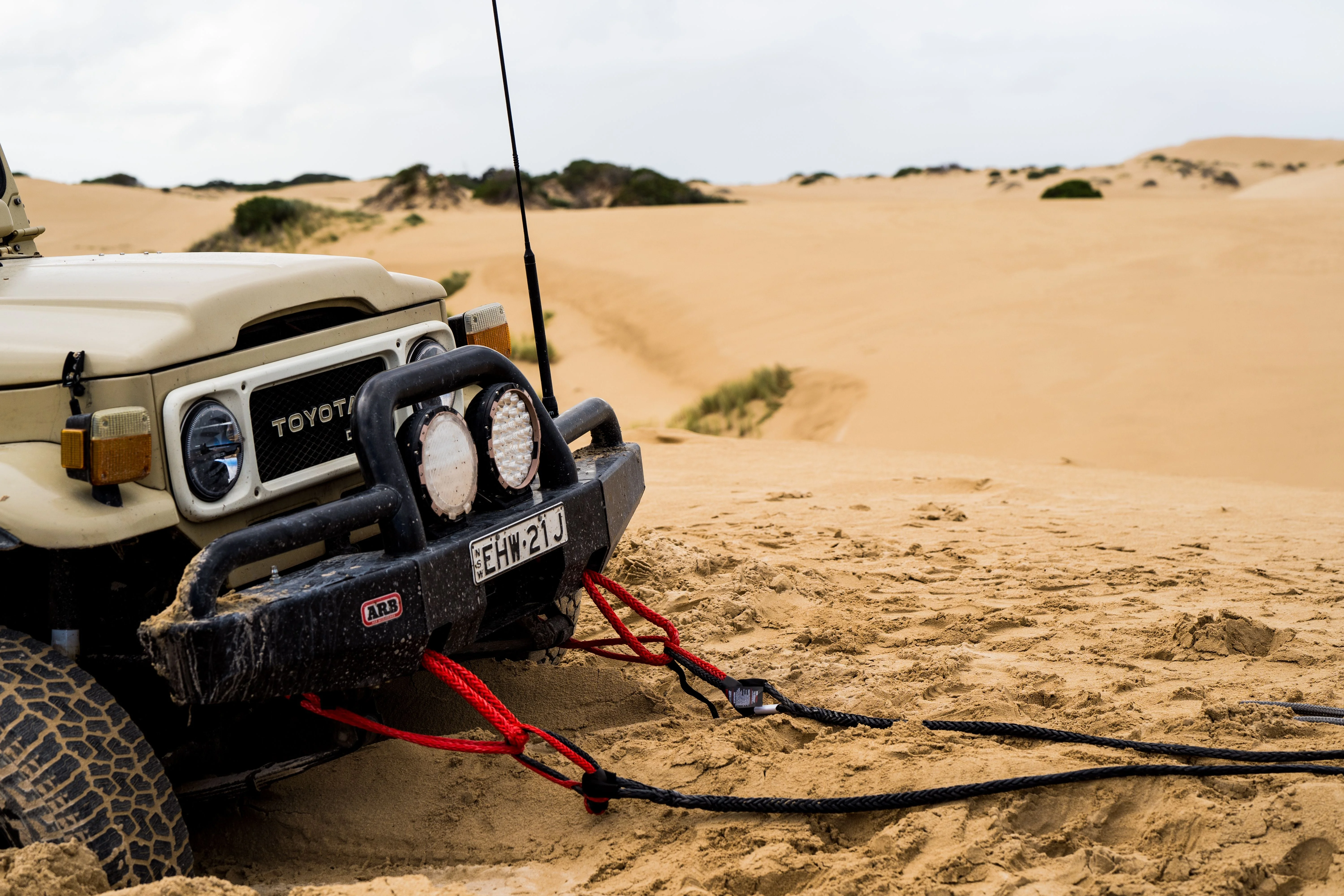 Red SaberPro bridle rigged to the front bumper of a Toyota Land Cruiser, running back to a winch cable on sand dunes