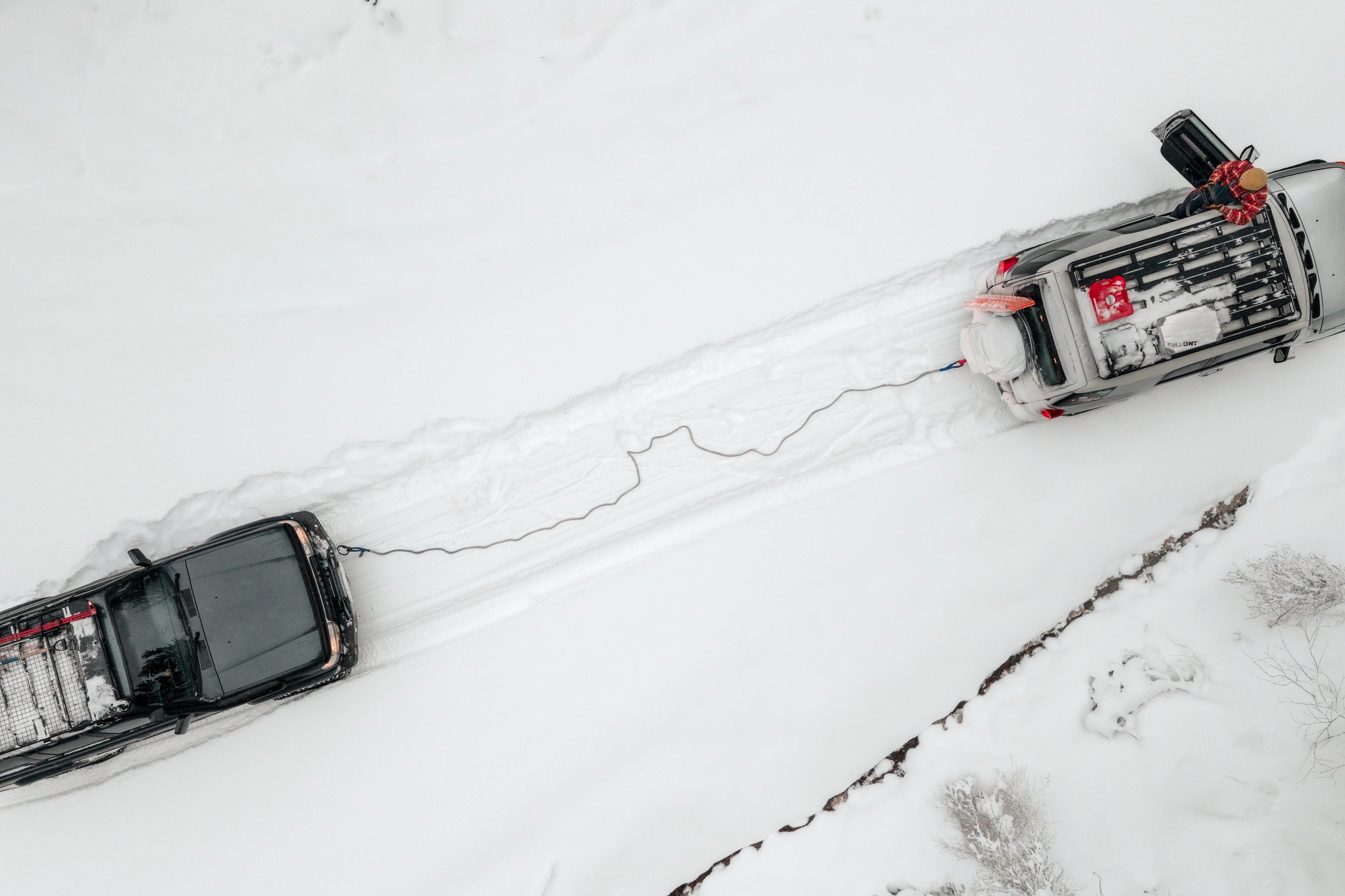 Aerial drone view of two 4WDs connected by a taut kinetic rope during a snow recovery